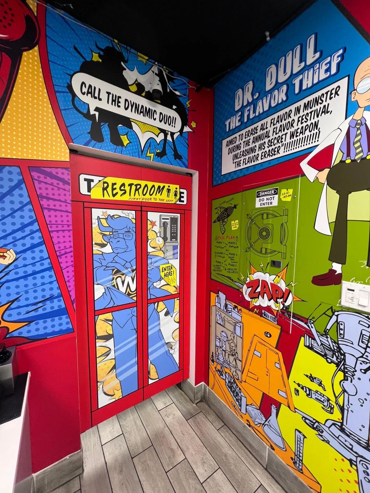 Comic-strip mural wrapping a restroom entrance: CALL THE DYNAMIC DUO and DR. DULL THE FLAVOR THIEF in bold pop-art panels.