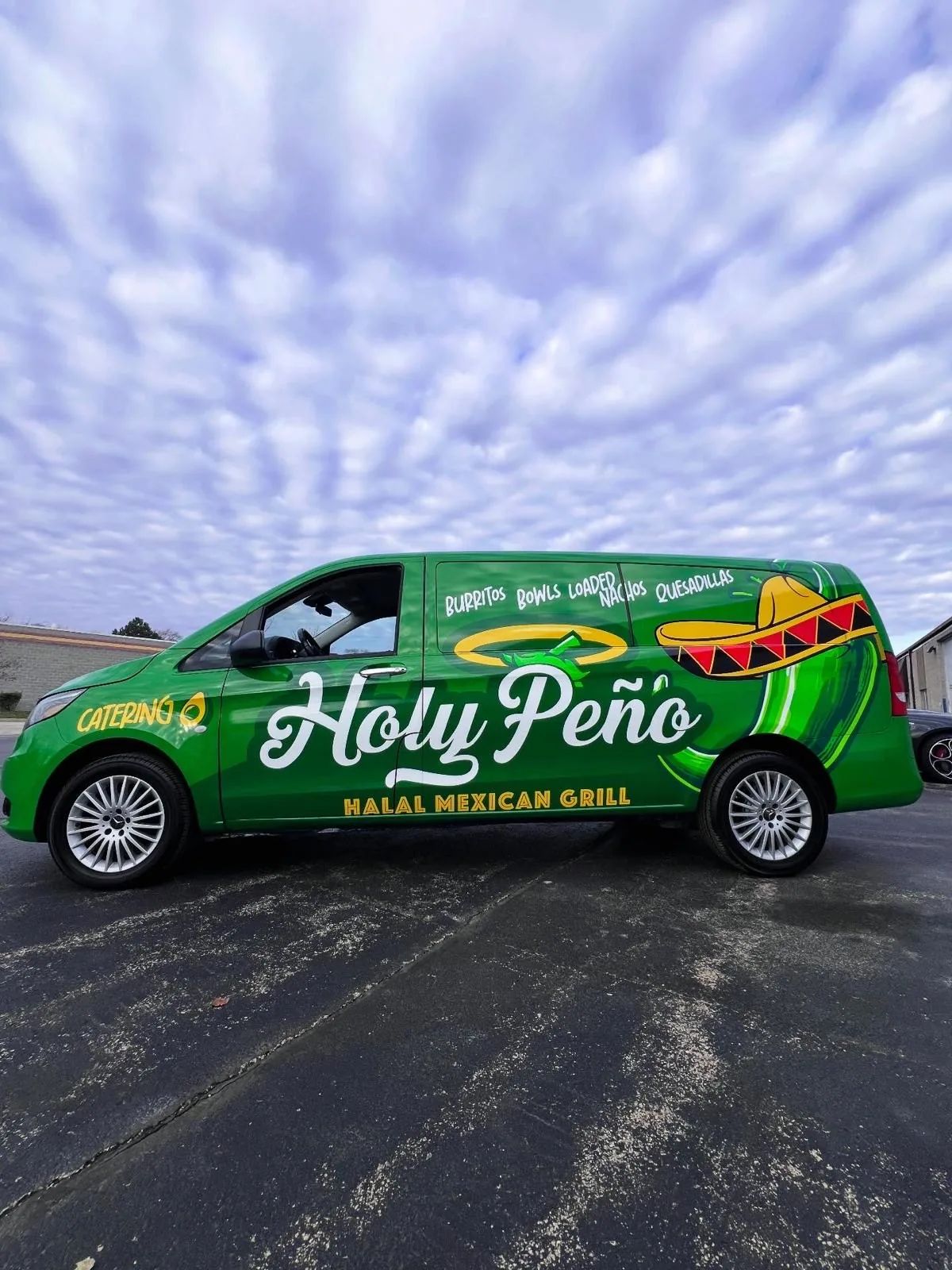 Green cargo van in a full Holy Peño wrap with the script logo and a sombrero graphic, parked under a cloudy sky.