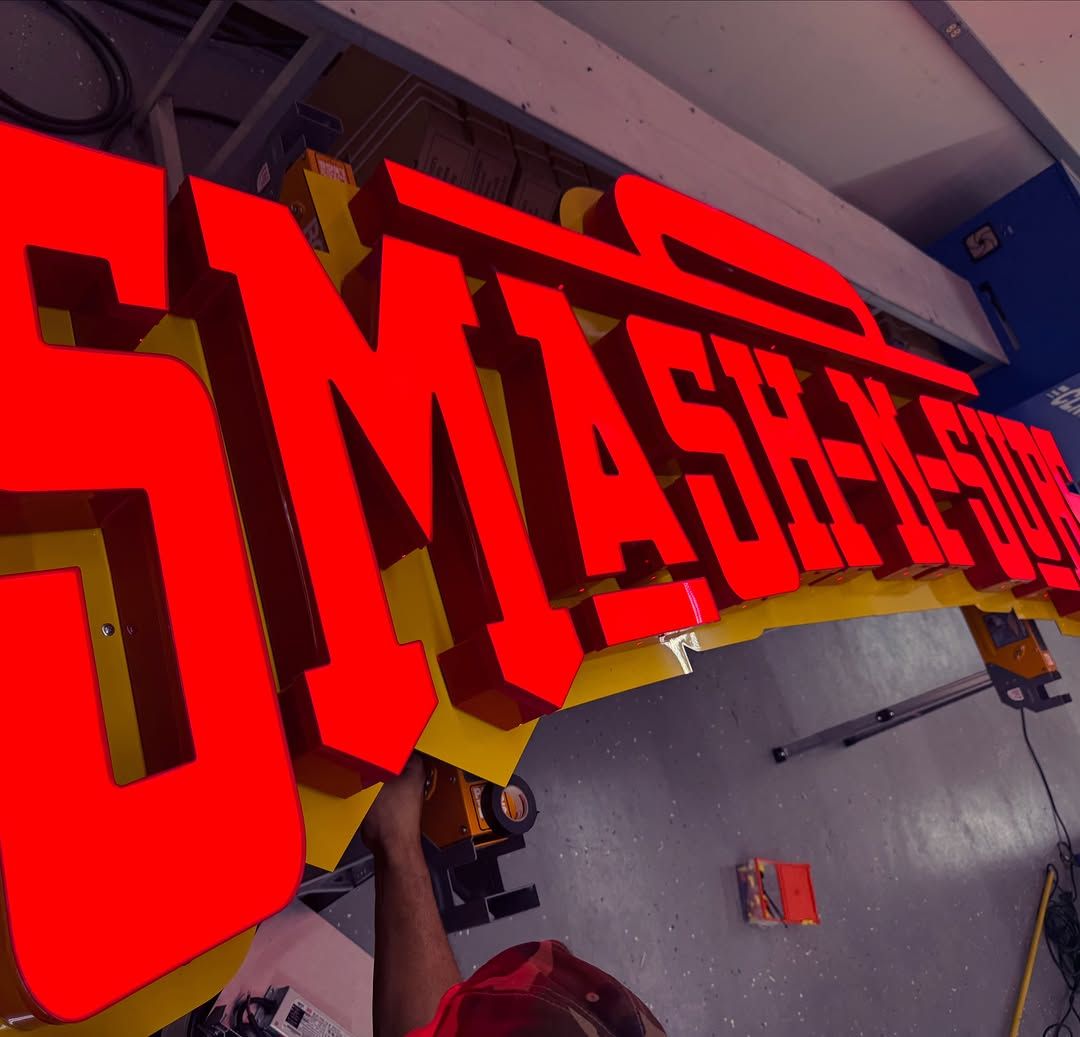Large red channel letters spelling Smash-N-Subs being assembled on a workbench.