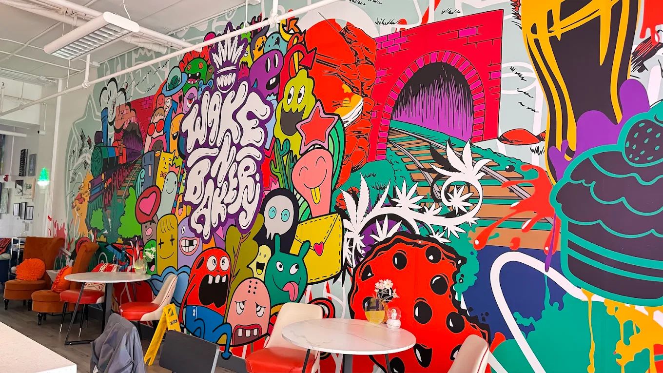 Bright printed mural of cartoon characters, a train and a brick tunnel covering the long wall of a café seating area.