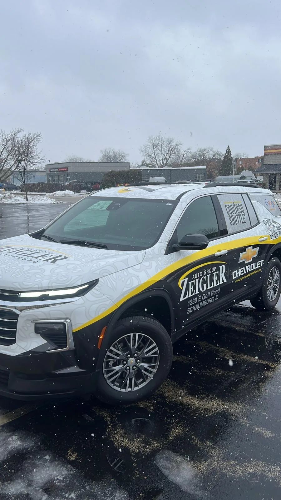 White Chevrolet Traverse with Zeigler Chevrolet dealer lettering and a yellow stripe wrap, in a snowy lot.