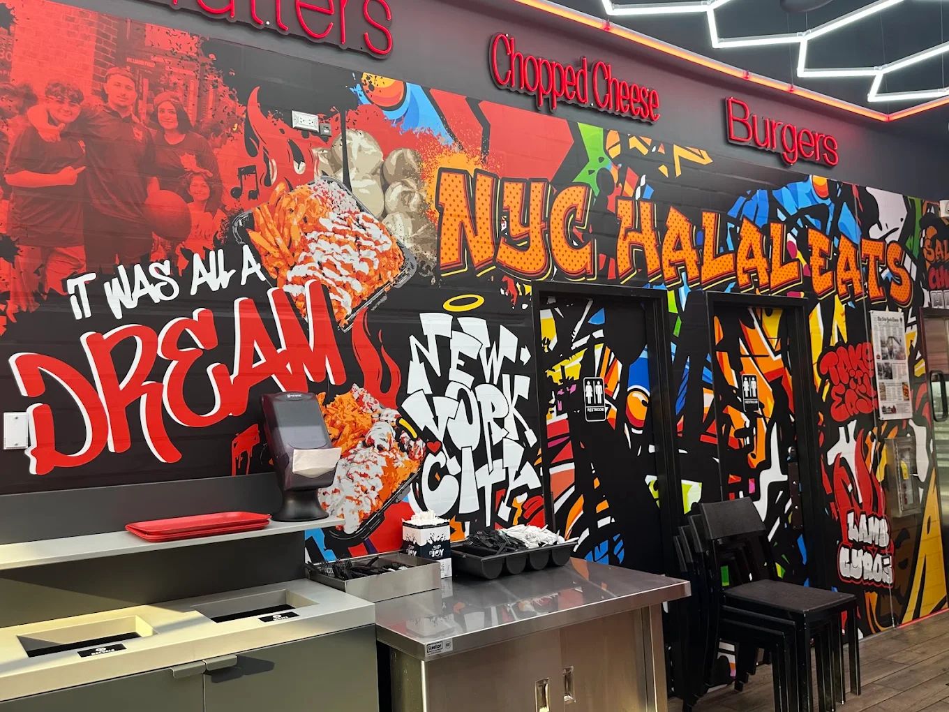 Full-wall printed mural inside NYC Halal Eats: graffiti lettering, food illustrations and red neon menu signs along the top.