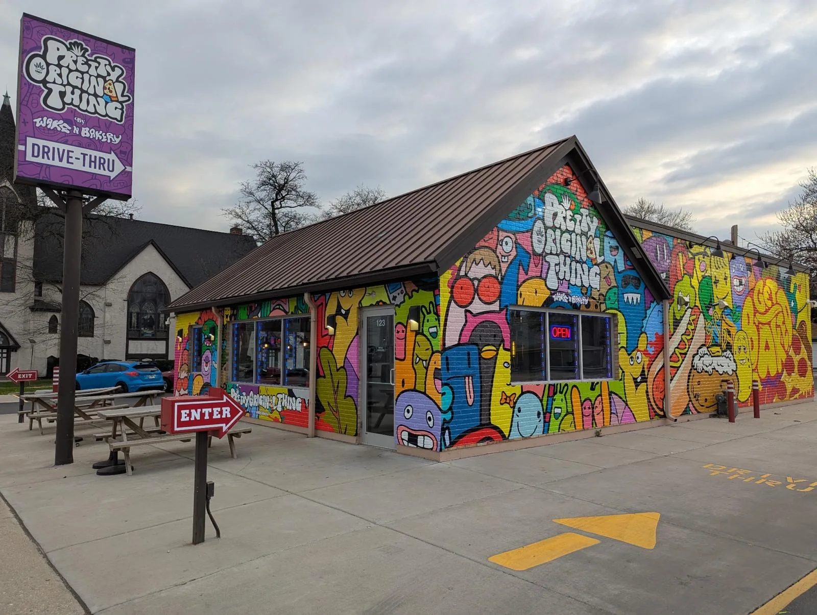 Wake n Bakery building covered in a printed doodle mural, with the drive-thru sign and an ENTER arrow on the lot.