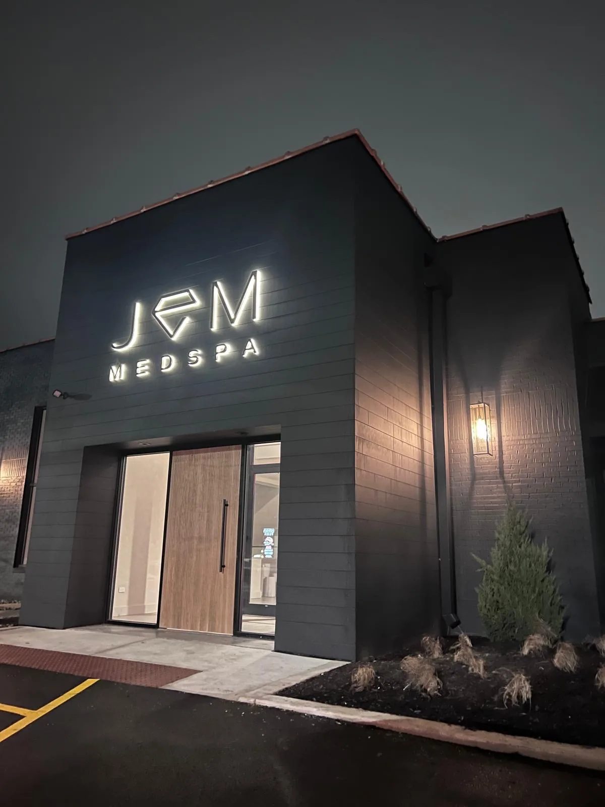 JEM Medspa at dusk: a dark modern building with its illuminated JEM MEDSPA sign glowing over the entrance.