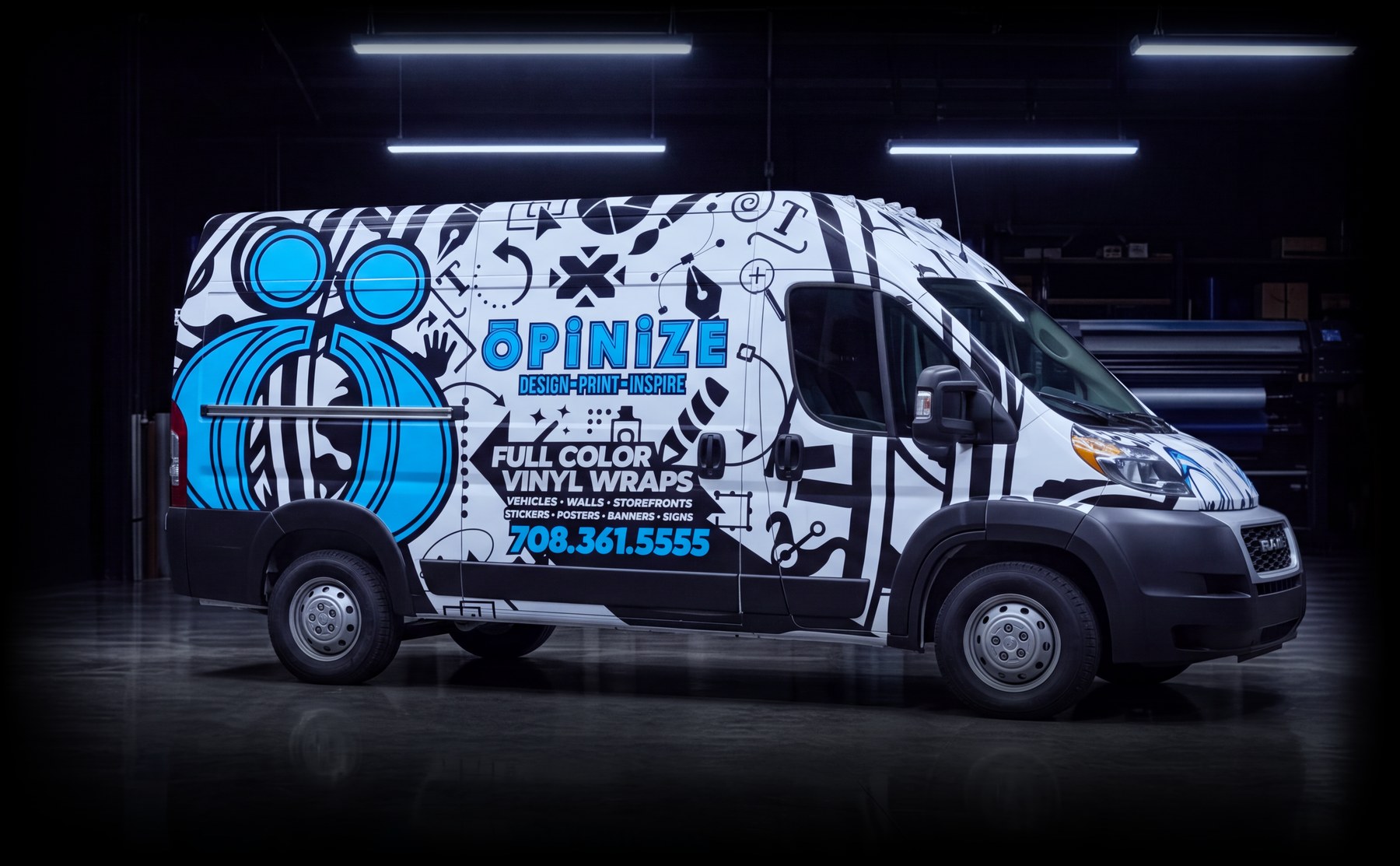 The Opinize Design van in its black, white and blue wrap with the shop's phone number, parked side-on in a garage bay under the lights