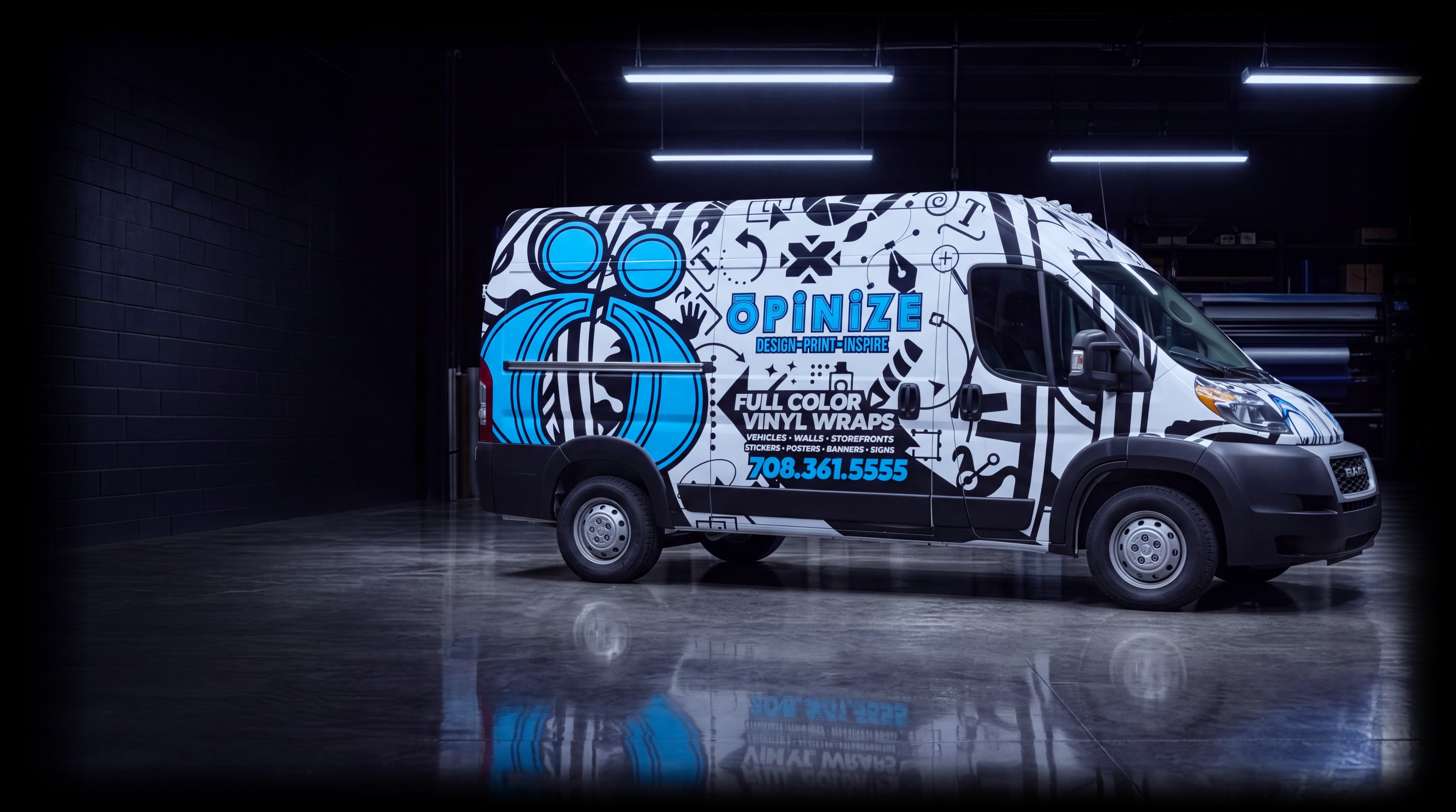 The Opinize Design van in its black, white and blue wrap with the shop's phone number, parked side-on in a garage bay under the lights
